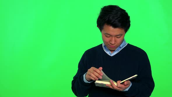 A Young Asian Man Reads a Book While Standing, Eventually Looks Up - Green Screen Studio