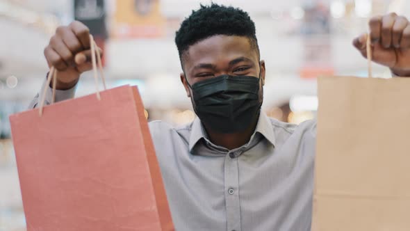 Closeup Happy Guy in Medical Mask Holds Paper Bags in Hands Boasts with Purchase Young African