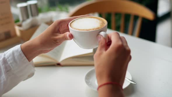 Beautiful Pretty Woman Raises White Porcelain Cup With Cappuccino Coffee. The Girl Is Sitting
