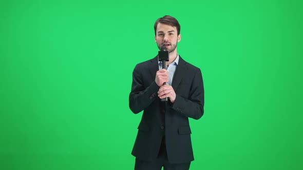 Man Reporter in Suit Looks Into the Camera and Speaks Into a Microphone on a Green Background a