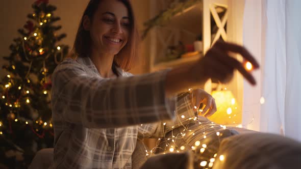 Portrait of Happy Dreaming Woman Decorating Couch with Xmas Lights
