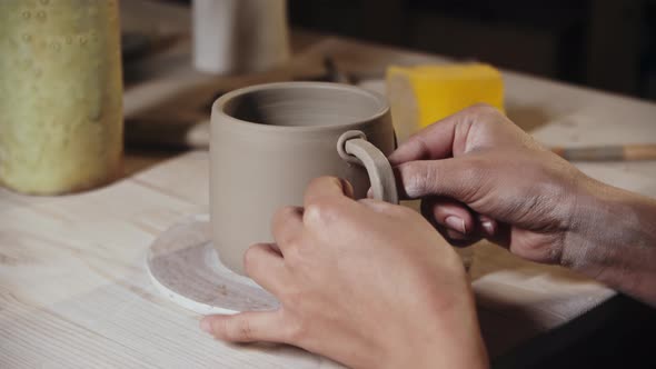 Young Woman Potter Attaching a Small Piece of Clay to an Edge of the Handle and a Cup