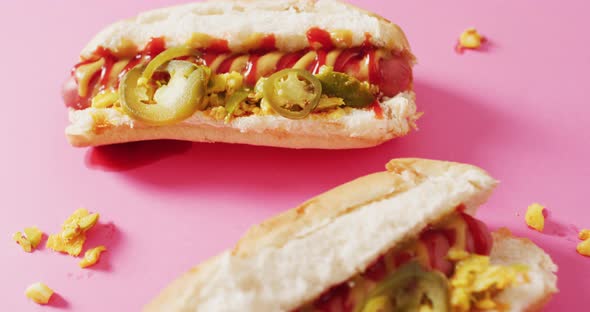 Video of hot dogs with mustard, ketchup and jalapeno on a pink surface