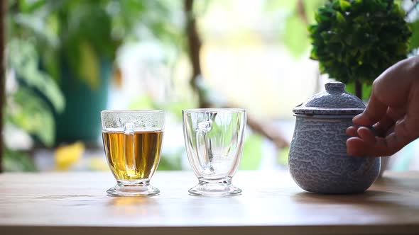 An adult hand pour hot tea into cups on the table in the morning