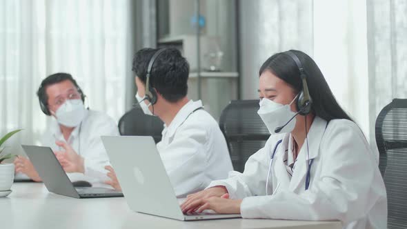 Woman Doctor In Mask Working As Call Centre Agents Speaking On A Call While Colleagues Are Talking