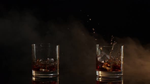 Barmans Dropping Ice Cubes Into Drinking Glasses with Whiskey Cognac Brandy on Black Background