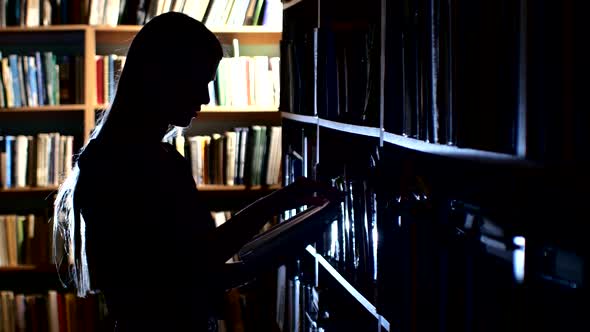 Pretty Young College Student in a Library, Chooses a Book. Close Up, Back Light