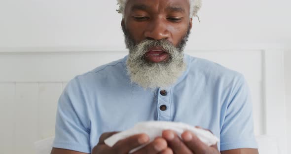 Senior man with tissue sneezing in bed at home