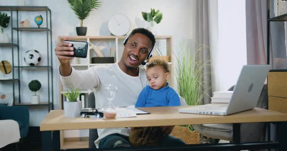 Black-Skinned Father in Headset Making Selfie Together with His Small Son at Home