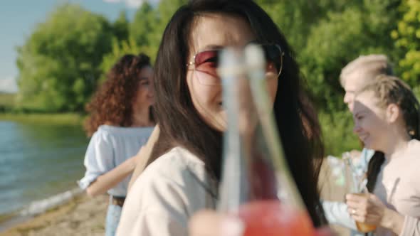 Portrait of Happy Asian Girl Wearing Sunglasses Dancing on Beach Holding Bottle with Drink