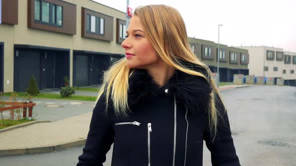 A Young Beautiful Woman Stands on the Street in a Suburban Area and Looks Around