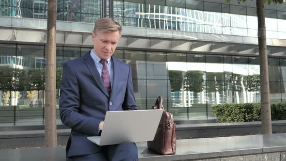 Pensive Businessman Sitting Outside and working on Laptop