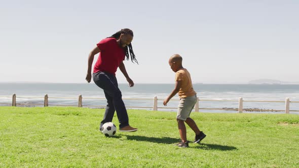 Video of happy african american father and son playing soccer outdoors and having fun