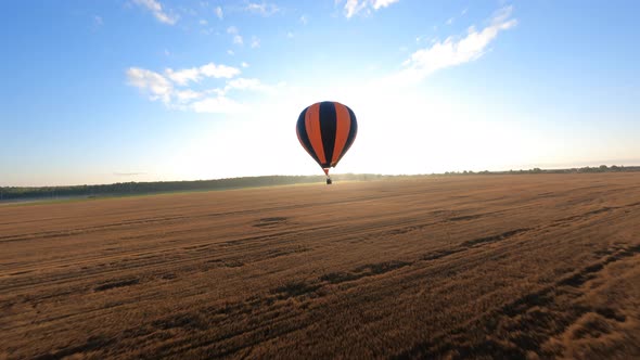 Orange Hot air ballon floating above sloping field at beautiful sunrise