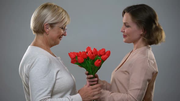 Caring Daughter Giving Red Tulips to Mature Mother, International Women Day