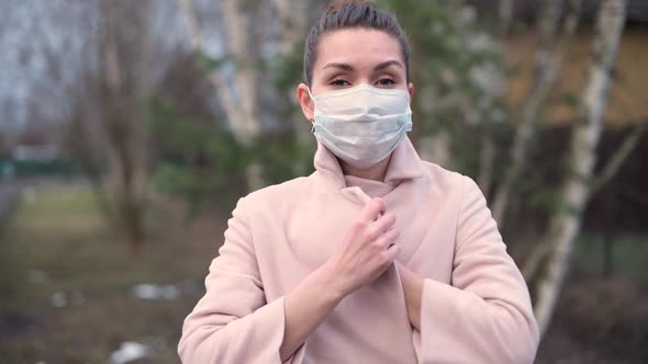 woman in medical mask wraps herself in a coat on the street