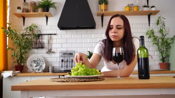 Relaxed Young Woman Poses with Glass of Red Wine Standing at Kitchen Table