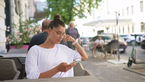 Beautiful Young Woman Sitting in Street Cafe Using a Smartphone