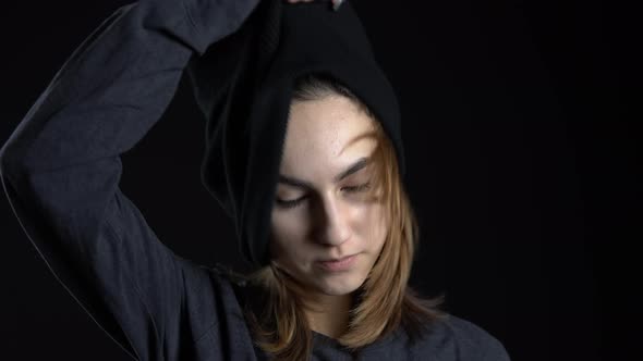 A Young Woman Takes Off the Mask of a Balaclava. Bandit on a Black Background Close-up.