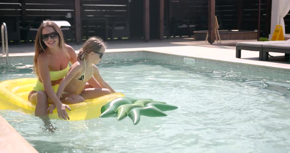 Mother and Daughter with Inflatable Pineapple Mattress in Swimming Pool