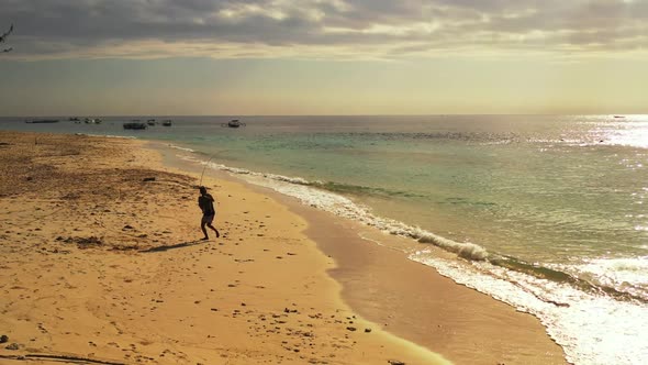 Boy fishing on marine resort beach break by shallow ocean and white sand background of Gili Air near