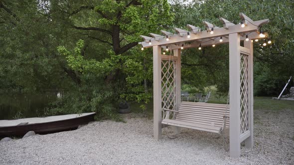 Beautiful Large Wooden Swing Stands on Rocky Shore with Trees Near Pond