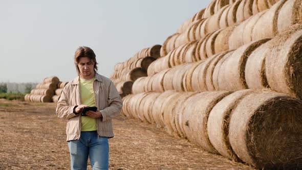 Farmer Agronomist Checks Hay Bales on the Wheat Field After Harvest at Sunset