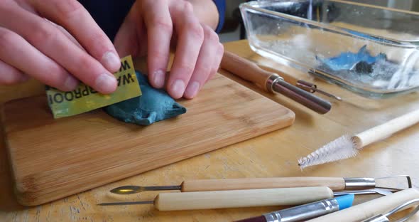 An artist in a messy studio using wet sandpaper while sanding and polishing a polymer clay sculpture