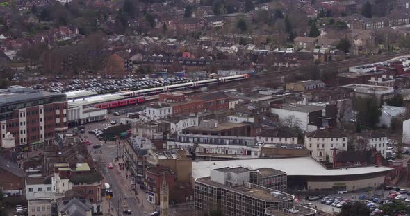 Wide aerial view tracking a commuter train passing through Surbiton train station, London, UK