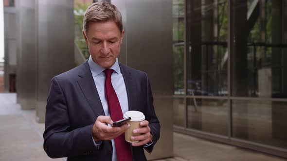 Businessman walking to work using smart phone with takeaway coffee