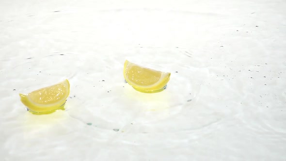 Half a Lemon Falls Into the Water and Flies To Two Quarters. White Background. Slow Motion