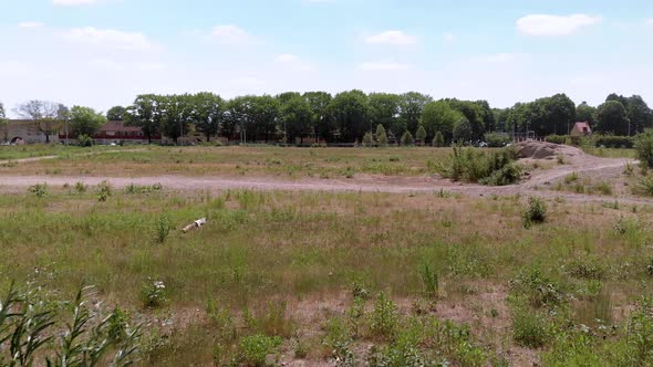 drone view of a undeveloped wasteland full of weeds, grass and sand, shot from behind a bush