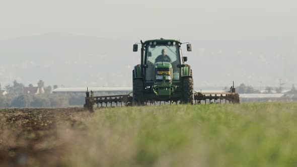 Tractor cultivating a green field in slow motion.