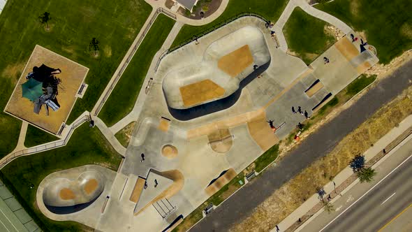 Ascending rotating aerial view of a community skate park with kids on skateboards and scooters in su