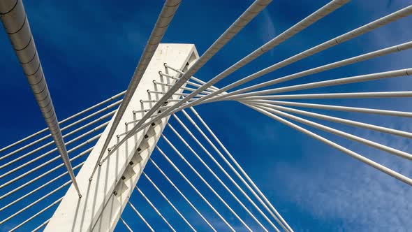 Pylon of a cable stayed bridge under fast moving white clouds in blue sky supported by ropes lines