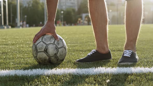 Man with Hairy Legs Takes an Old Soccer Ball with Hand Closeup
