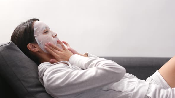 Woman applying facial mask and lying on sofa 
