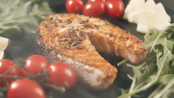 A Cooked Salmon Steak with the Addition of Aromatic Spices and Vegetables on a Black Serving Plate