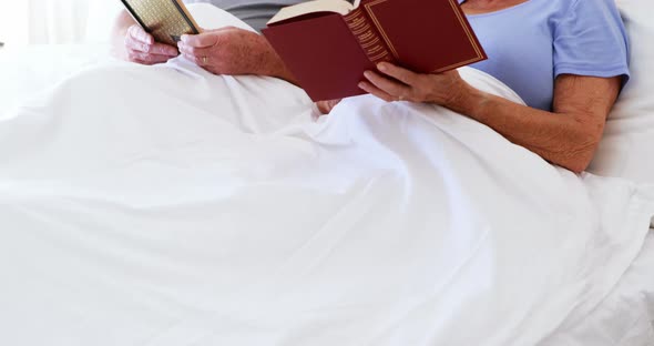 Happy senior couple reading book on bed