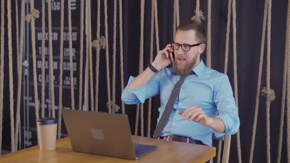 Male Business Owner Is Sitting in Office and Talking By Mobile Phone Cheerfully