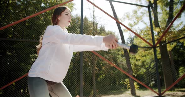 Young and Beautiful Girl Lifts Weights Outside at the Sports Field