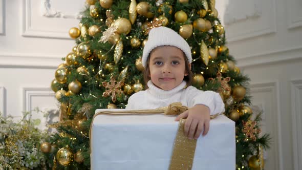 Boy Child in a White Sweater and Hat Stands at the Christmas Tree