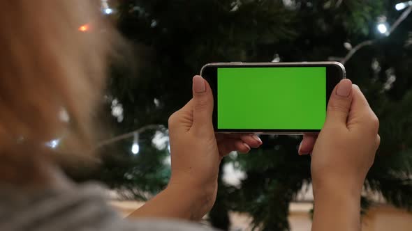 Female holds green screen gadget in front of Christmas tree 4K 2160p 30fps UltraHD footage - Greensc