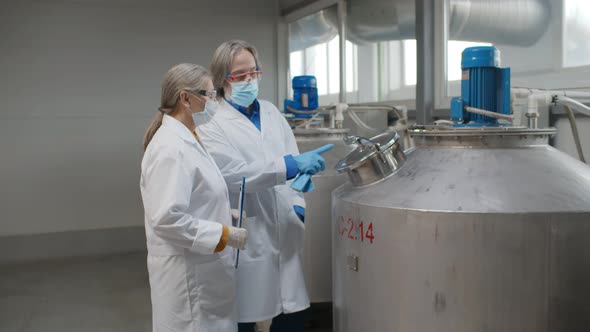 Senior Woman and Man Specialists in Safety Mask and Gloves Making Inspection of Production Line