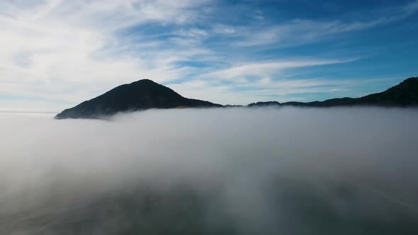 AERIAL: Ascending over a floor of fog to reveal a mountain on the Oregon coast.