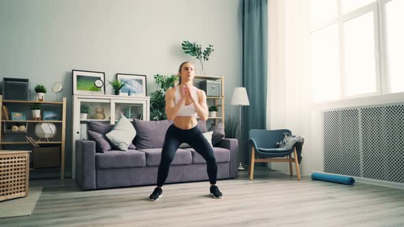 Girl Is Practising at Home Squatting and Raising Arms Exercising in Living Room