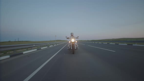 Woman in Helmet Rides Along Highway Evening on Motorcycle with Headlights on Front View