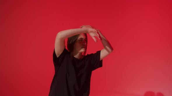 Young Woman Wearing Black Tshirt Dancing Contemporary on Red Neon Background in Studio