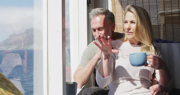 Happy caucasian mature couple drinking coffee and talking in sunny living room