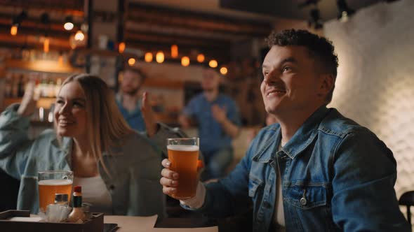 Closeup of a Group of Male and Female Friends Sitting Together in a Bar and Watching a Broadcast on